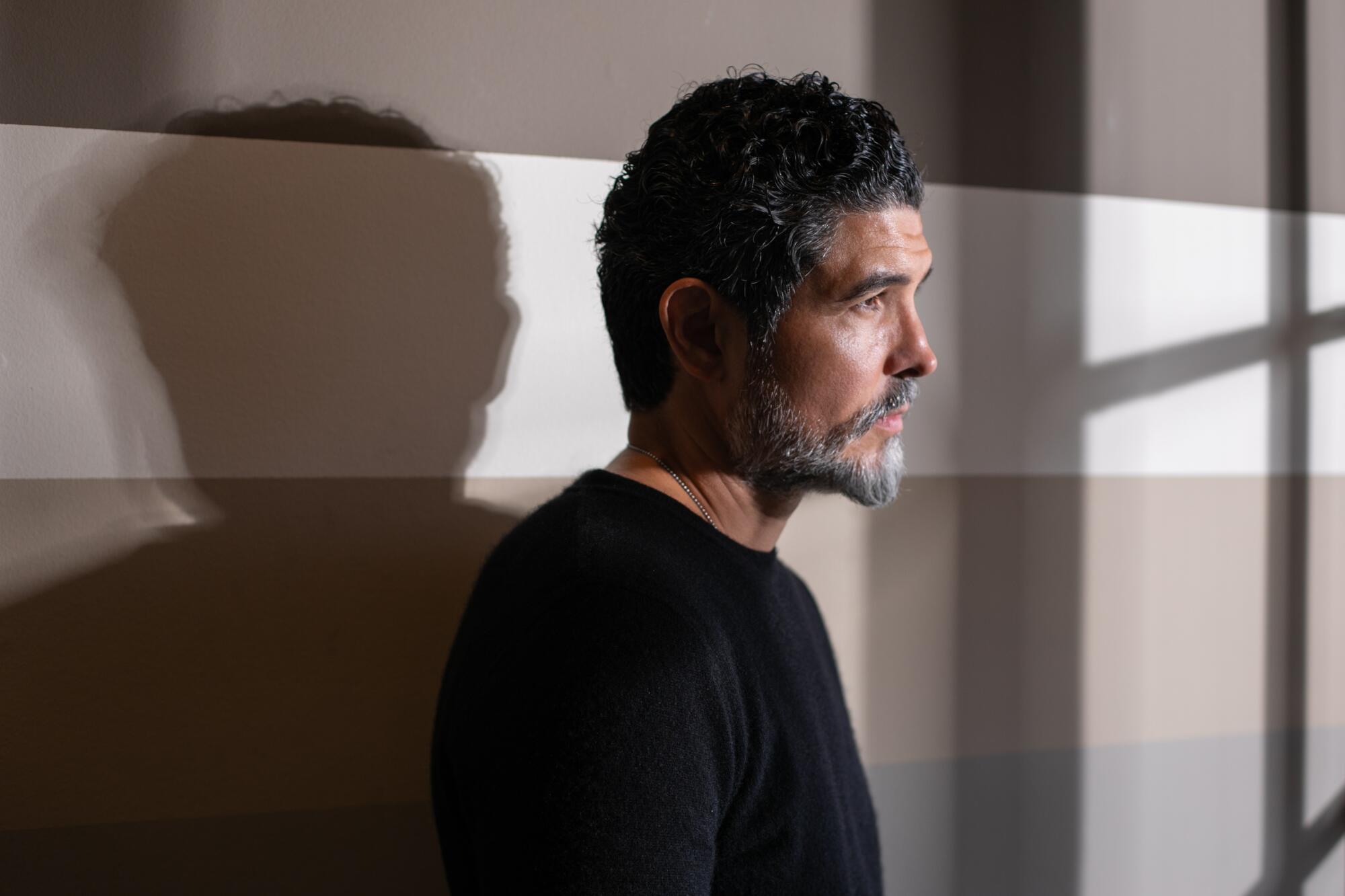 A man with a salt-and-pepper beard poses against a striped backdrop in shadows.