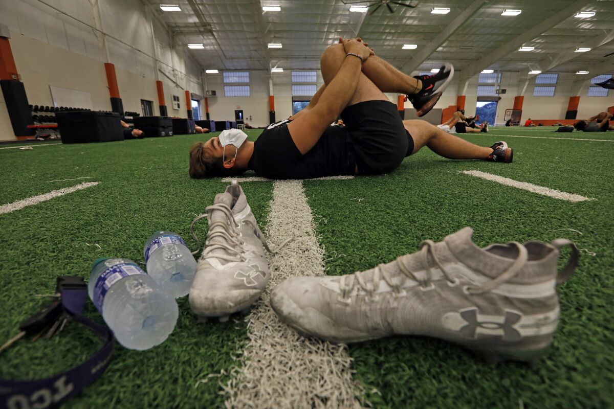 Kyle Thompson wears a mask while stretching during football practice at an indoor high school facility in Texas