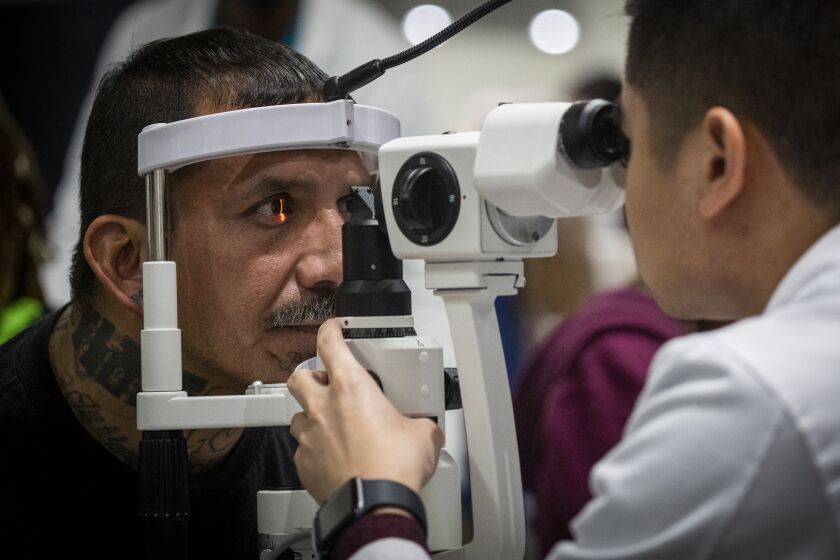 LOS ANGELES, CALIF. -- FRIDAY, NOVEMBER 15, 2019: Michael Poblete, right, a optometry student at Western University, right, performs an ocular health exam on Daniel Duenas, of Los Angeles, at Care Harbor, a volunteer-based healthcare charity, on the first day of the 11th annual Care Harbor L.A., a three-day clinic that provides thousands with healthcare to those with limited or no access to healthcare at The Reef in Los Angeles, Calif., on Nov. 15, 2019. More than 700 Healthcare Professionals are scheduled to volunteer their services. (Allen J. Schaben / Los Angeles Times)