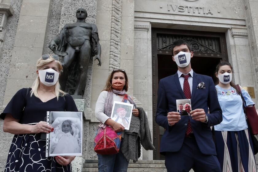 From left, Laura Capella, Nicoletta Bosica, Stefano Fusco and Arianna Dalba holds pictures of their relatives, victims of COVID-19, as they stand in front of Bergamo's court, Italy, Wednesday, June 10, 2020. Members of an association of relatives of COVID-19 victims filed a complaint with prosecutors seeking responsibility for the deaths of their loved ones. (AP Photo/Antonio Calanni)