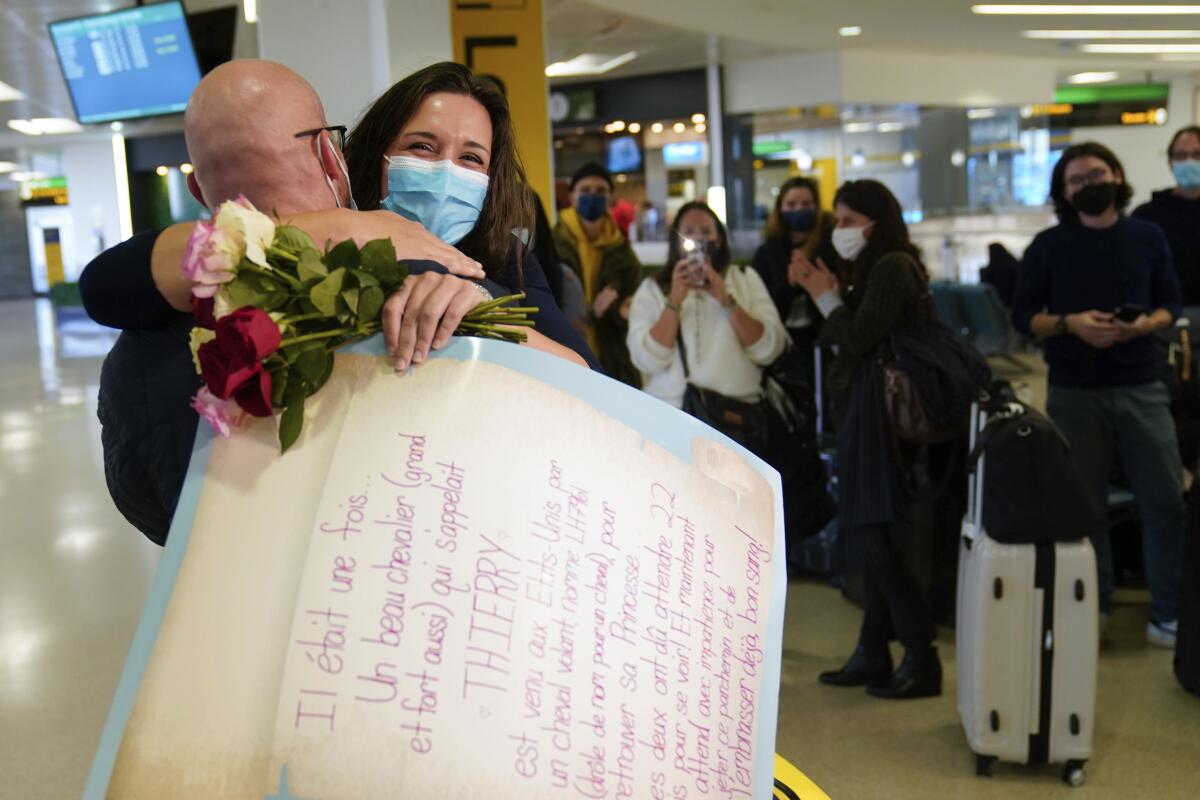 A woman and a man in masks embrace. The woman is holding roses and a large sign.