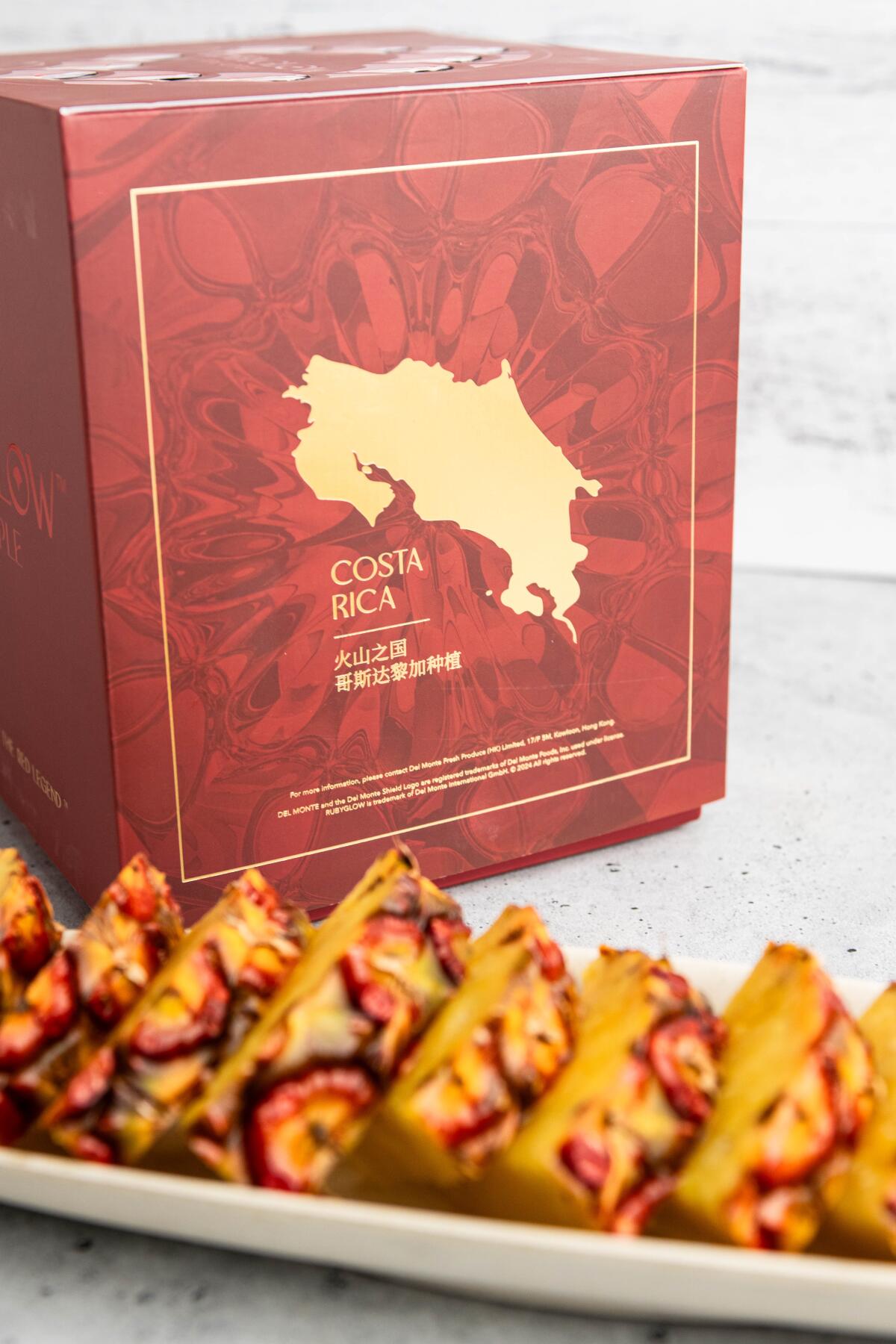 Slices of Ruby Glow pineapple in front of its red and gold packaging.