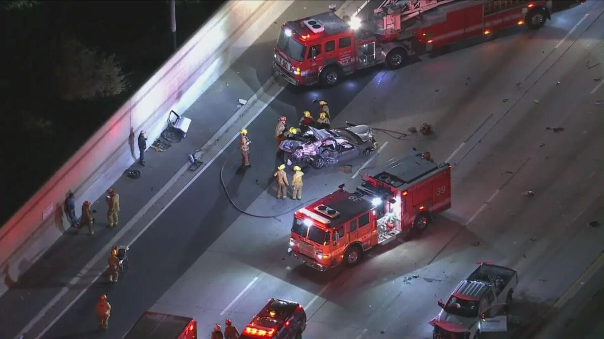 A crumpled car on a freeway is surrounded by fire trucks and rescue personnel.