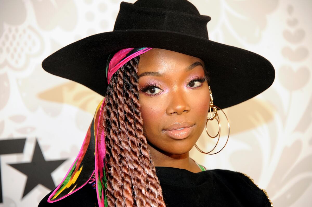 A woman with thick brown braids accented with pink and a big black hat