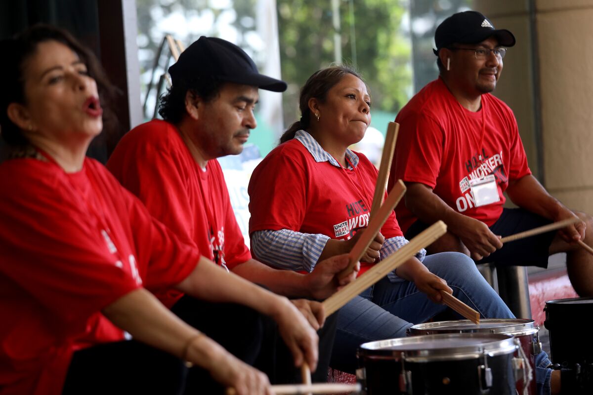 Four people sit while beating drums. 