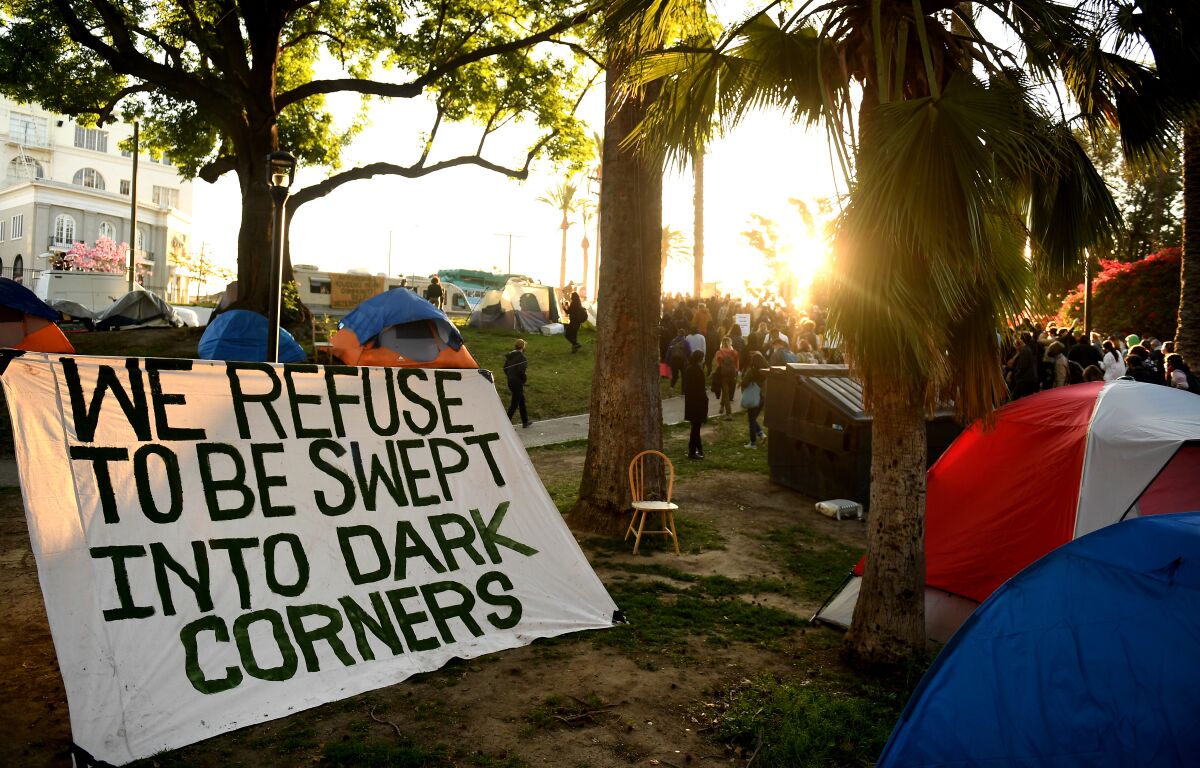 A sign that reads "We refuse to be swept into dark corners" sits among tents for homeless people during a rally.