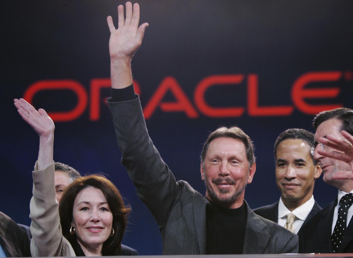 Larry Ellison waving and smiling with Safra Catz. 