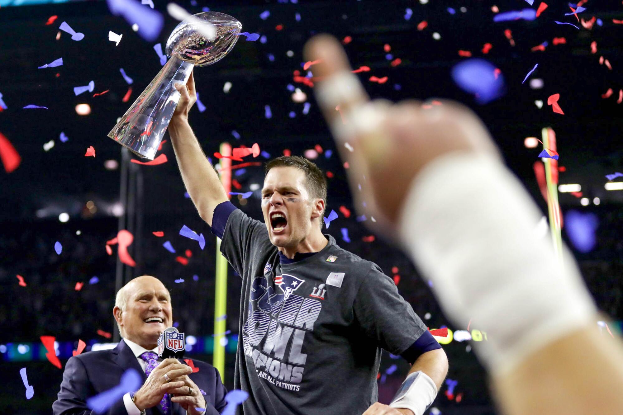 Tom Brady holds the Lombardi Trophy over his head as broadcaster Terry Bradshaw watches after the Patriots' Super Bowl win.