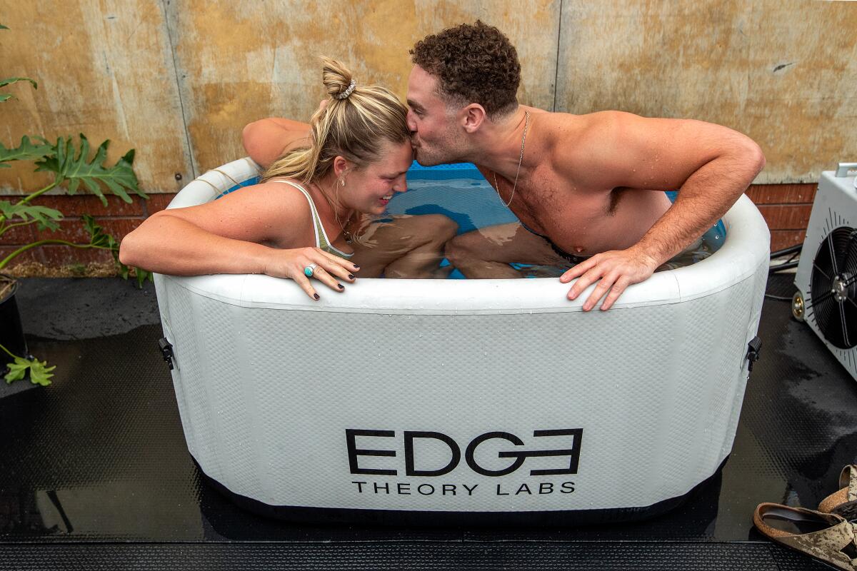 A man kisses a woman on the forehead as they sit in a tub of ice