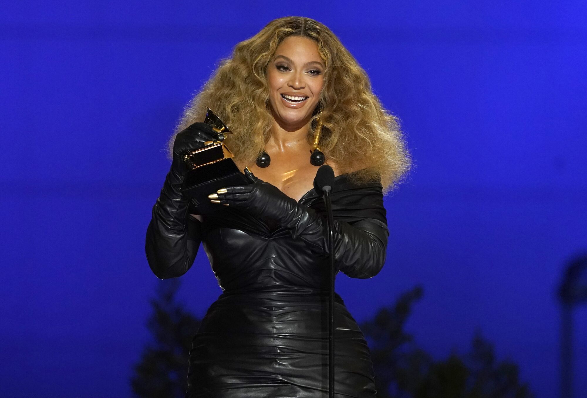 A woman in a black leather dress accepts an award on stage.