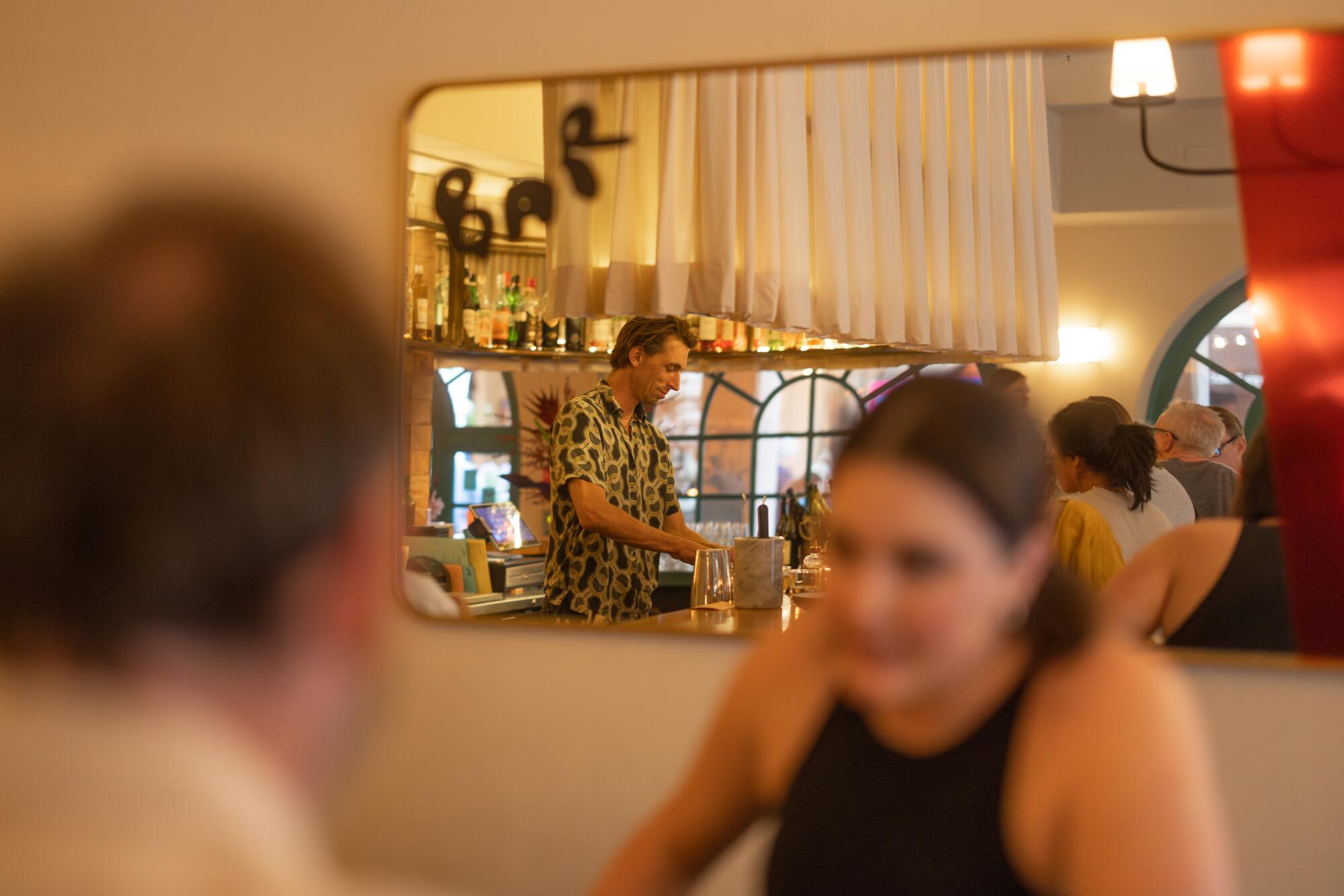 A couple dines at Bar Chelou as a bartender prepares drinks in the mirror reflection.