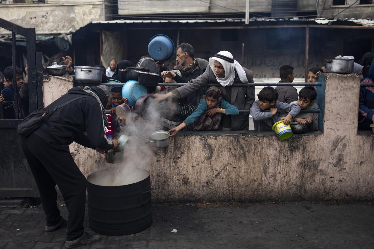 Palestinians line up behind a wall with bowls in hand for food distribution in Rafah, Gaza Strip