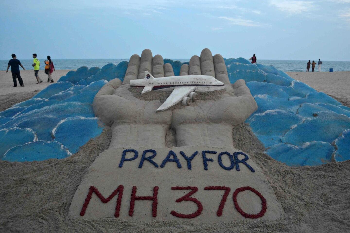 Beachgoers walk past a sand sculpture made by Indian sand artist Sudersan Pattnaik with a message of prayers for the missing Malaysian Airlines flight MH370.