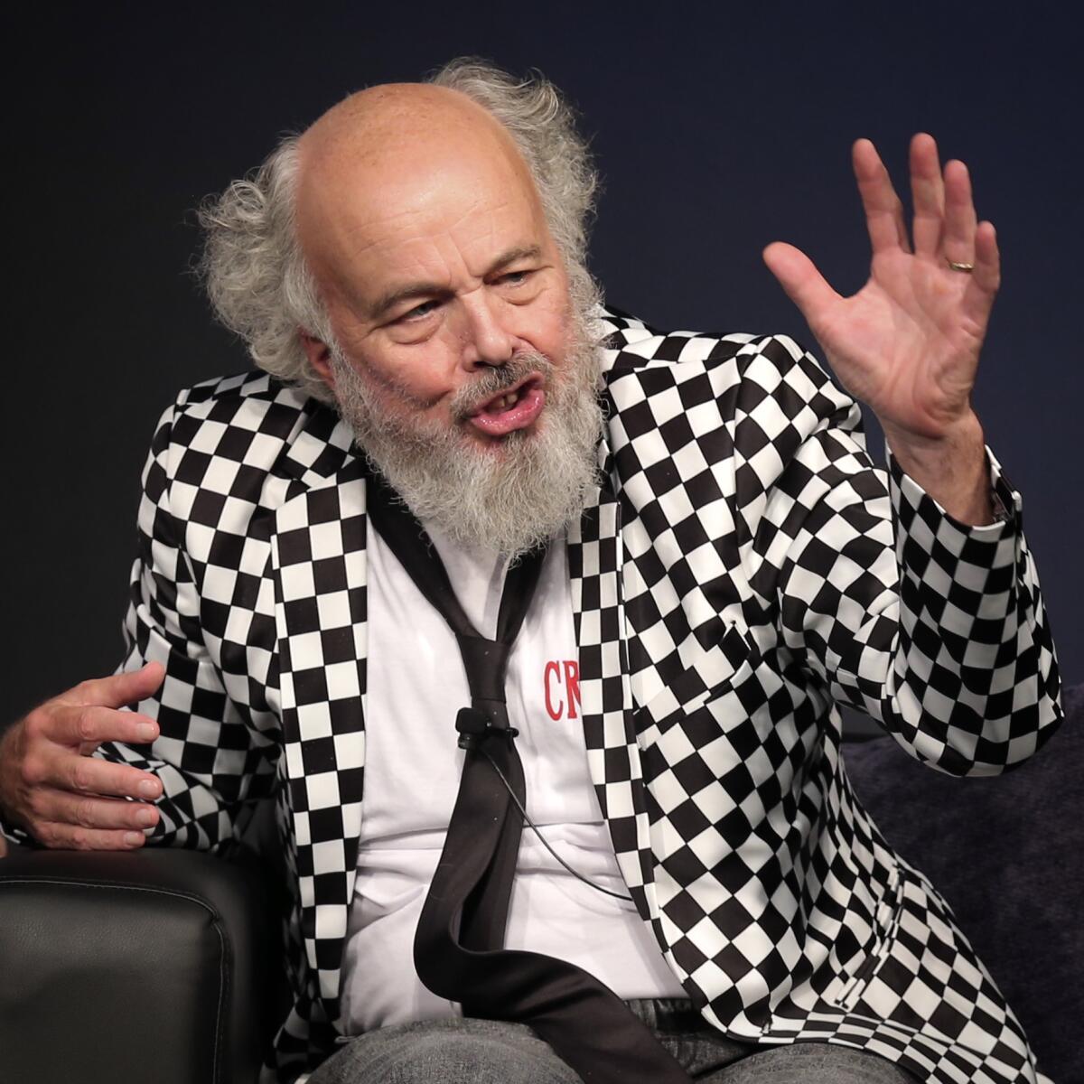 Clint Howard, in tie and checked jacket, gestures while speaking.