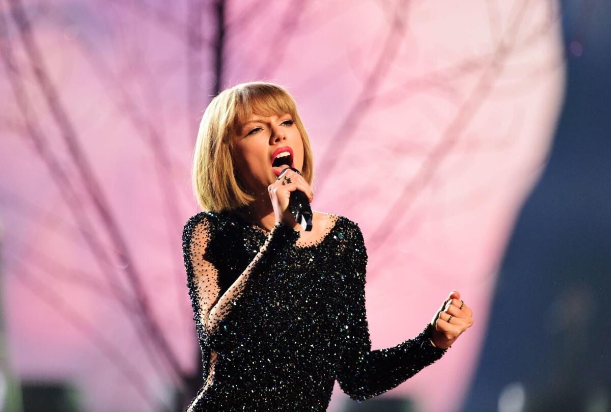 Taylor Swift sings onstage, wearing black and holding a microphone
