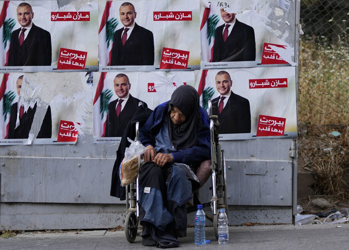 A homeless woman sits in front of campaign posters for a candidate in the upcoming parliamentary elections in Beirut, Lebanon, Monday, May 9, 2022. Given Lebanon's devastating economic meltdown, Sunday's parliament election is seen as an opportunity to punish the current crop of politicians that have driven the country to the ground. Yet a sense of widespread apathy and cynicism prevails, with many saying it is futile to expect change. (AP Photo/Hassan Ammar)