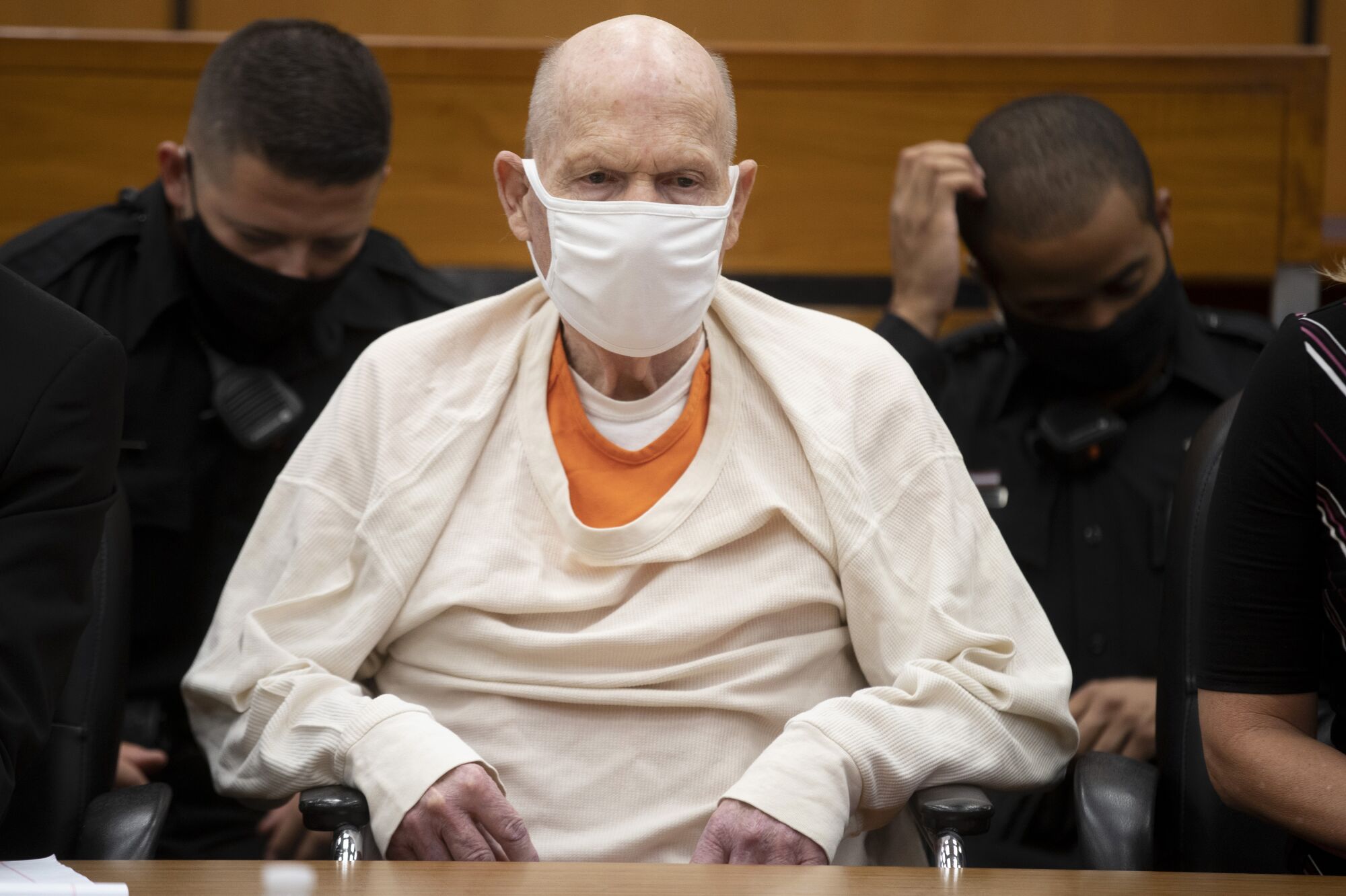 A masked Joseph James DeAngelo Jr. sits in a courtroom
