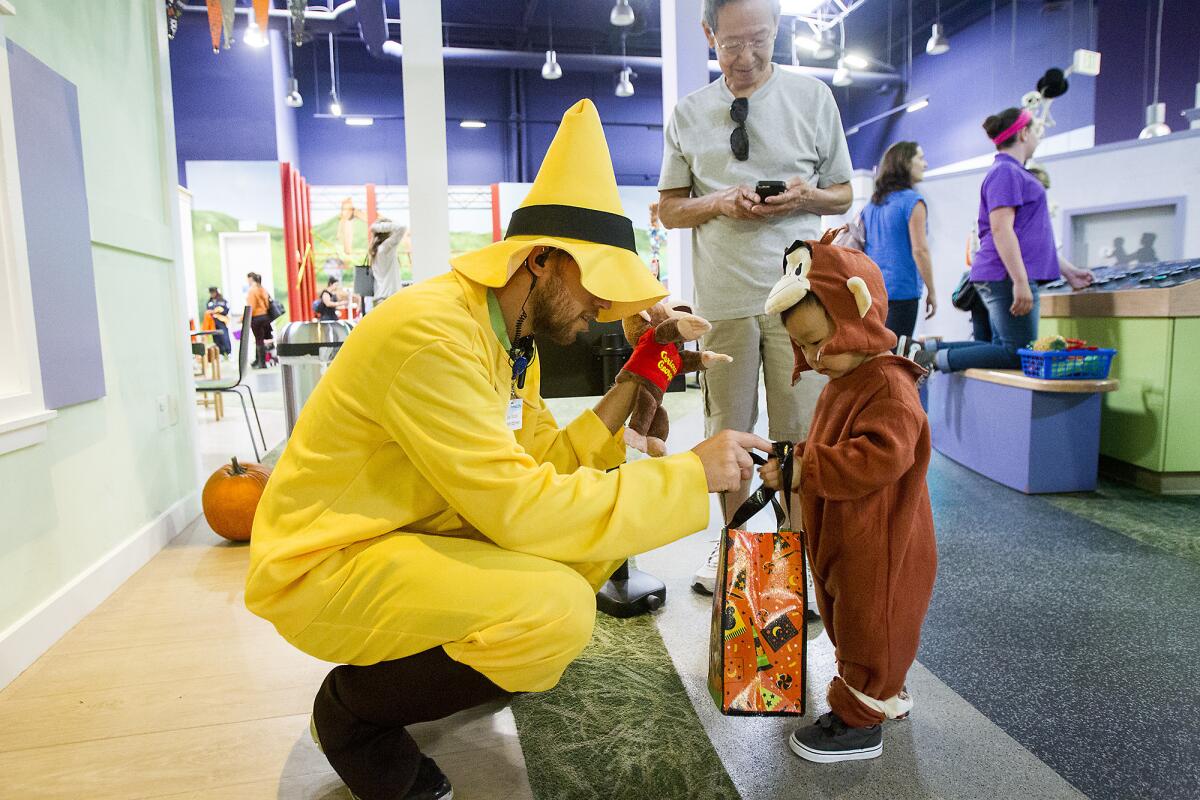Joel Wood, dressed as The Man in the Yellow Hat from the "Curious George" book series, gives a treat to Oliver Choi, 2, during Trick-Or-Treat Through the City event at Pretend City Children's Museum in Irvine on Friday, Oct. 31.