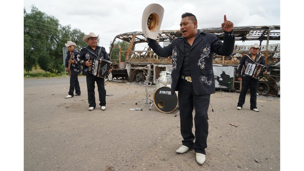 Ramon Gonzales Hernandez, the lead singer of Grupo Accion Oaxaca , a norteo band, performs in front of a burned-out bus at the entrance of Nochixtlan. (Liliana Niero del Rio / For The Times)