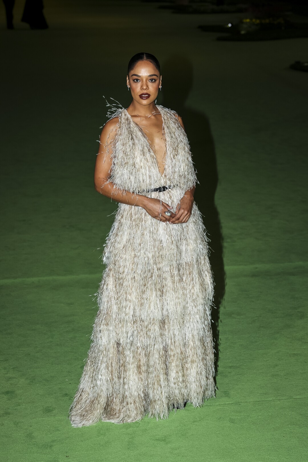 A woman in a feathery white dress posing on a green carpet