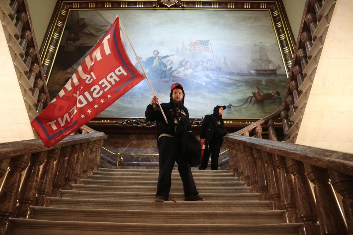 One of many militant Trump supporters who stormed the U.S. Capitol holds a Trump flag on a staircase near the Senate chamber.