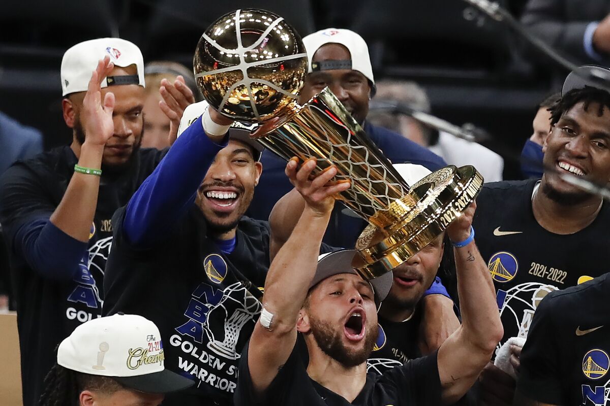 Golden State Warriors guard Stephen Curry holds up the Larry O'Brien Championship Trophy with teammates.