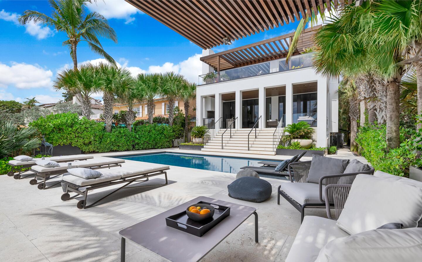The cabana is next to a pool and the house and has poolside furniture.