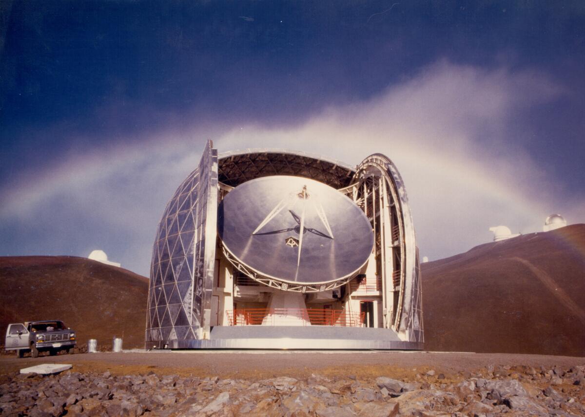A rainbow rises behind a gleaming observatory on a mountain summit.