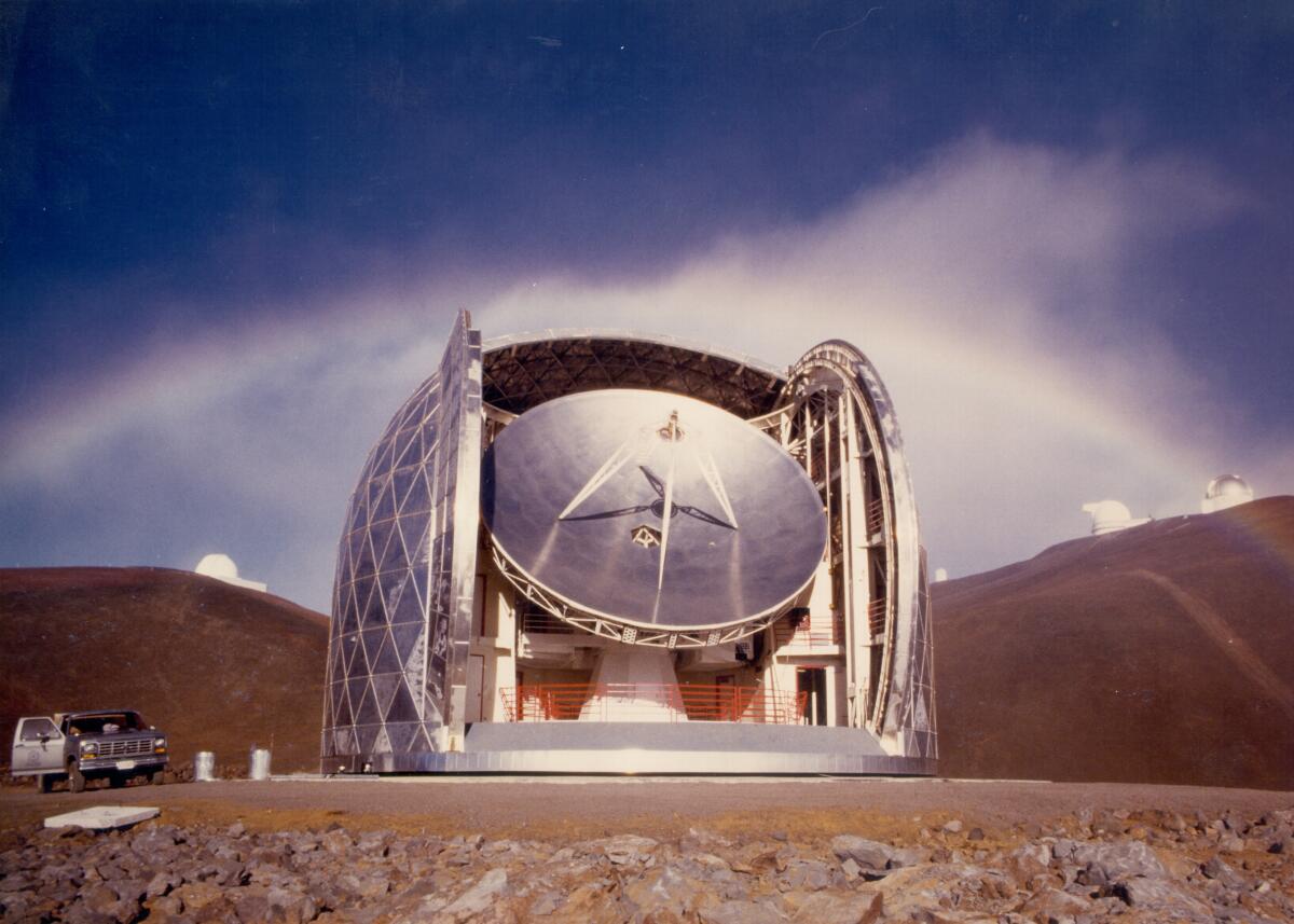 A rainbow rises behind a bright mountaintop observatory.