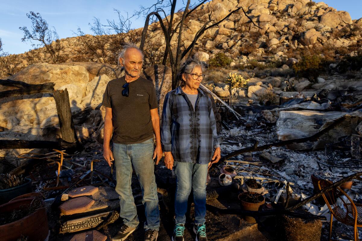 A couple stand amid rubble and ash.