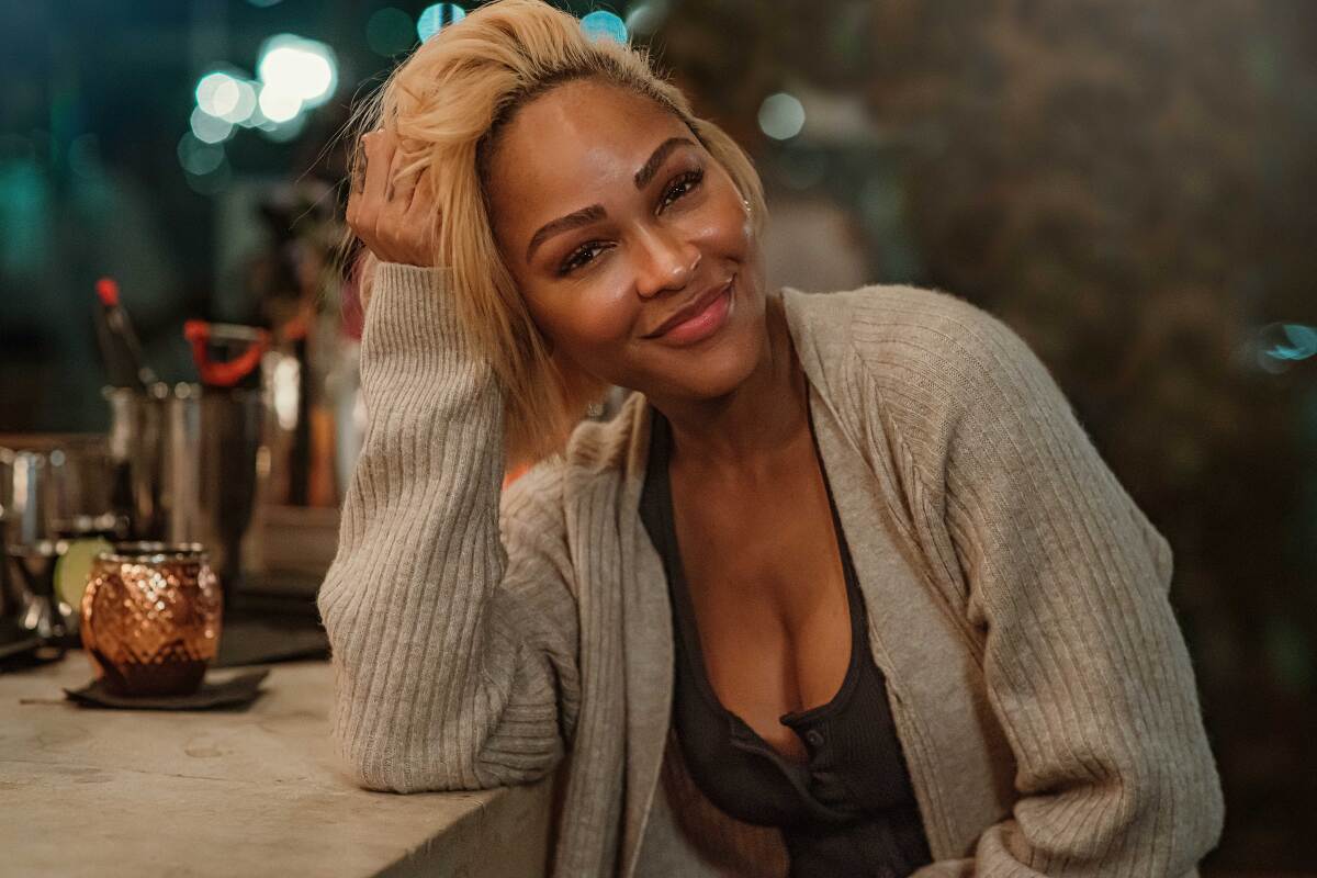 A woman in a brown cardigan leans on her arm at a bar