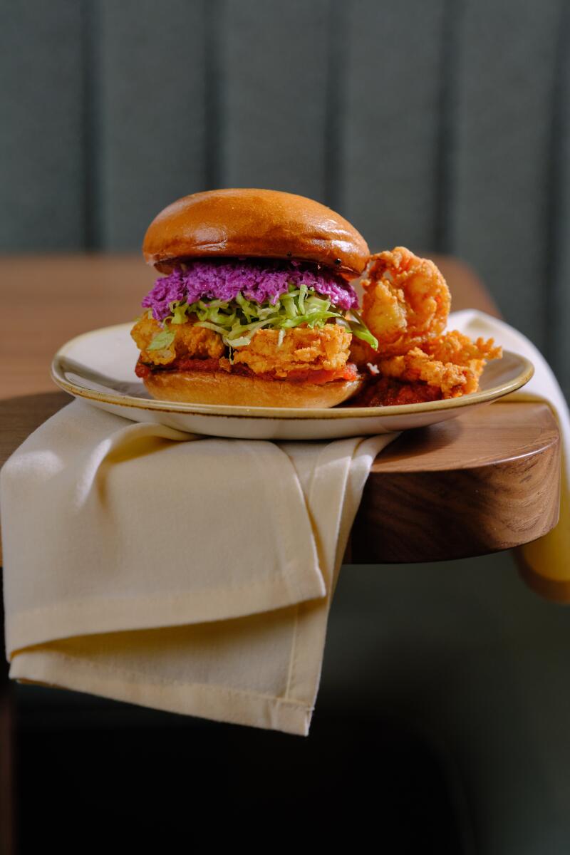 A side view of a fried shrimp sandwich on a plate, arranged with a napkin on a table.