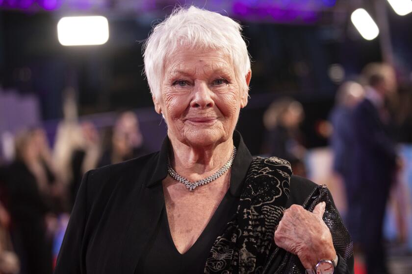 Judi Dench poses is posing for photographers wearing a black blazer with a black and gold patterned sash