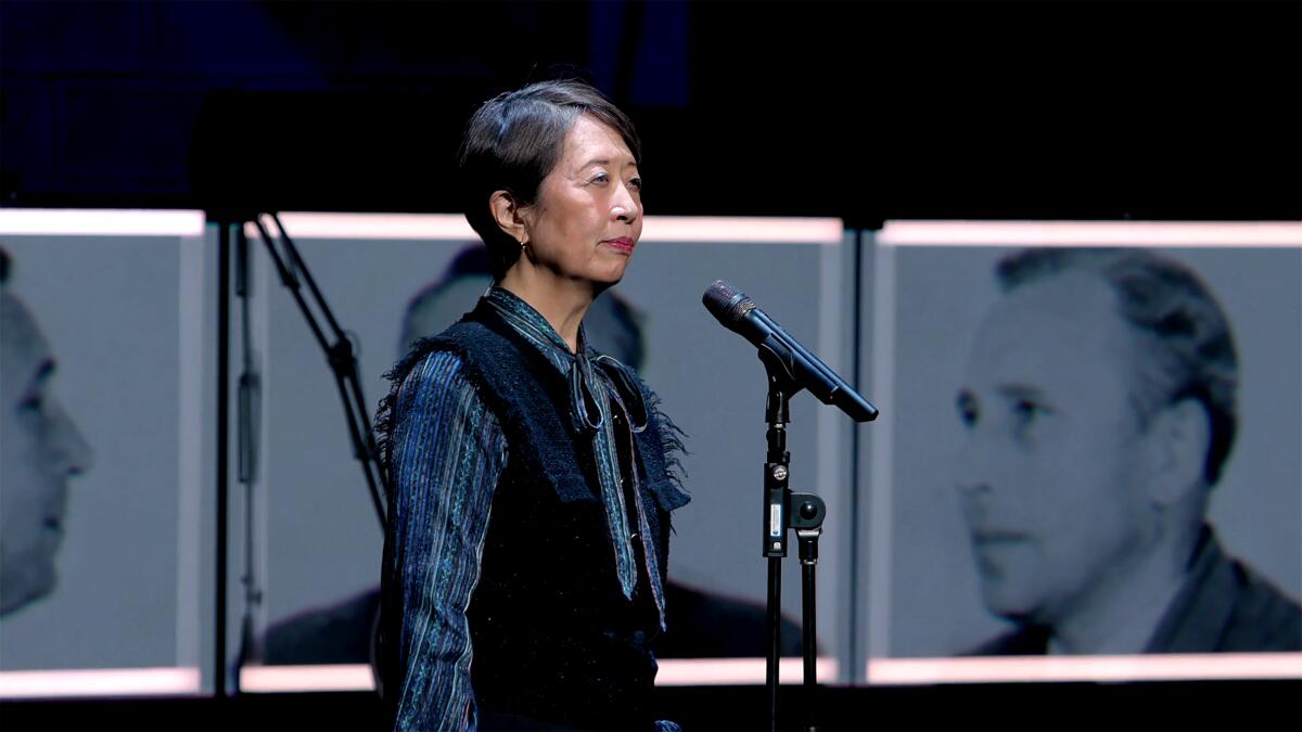A pistillate stands down a microphone stand, with black-and-white photos successful the background, connected stage.
