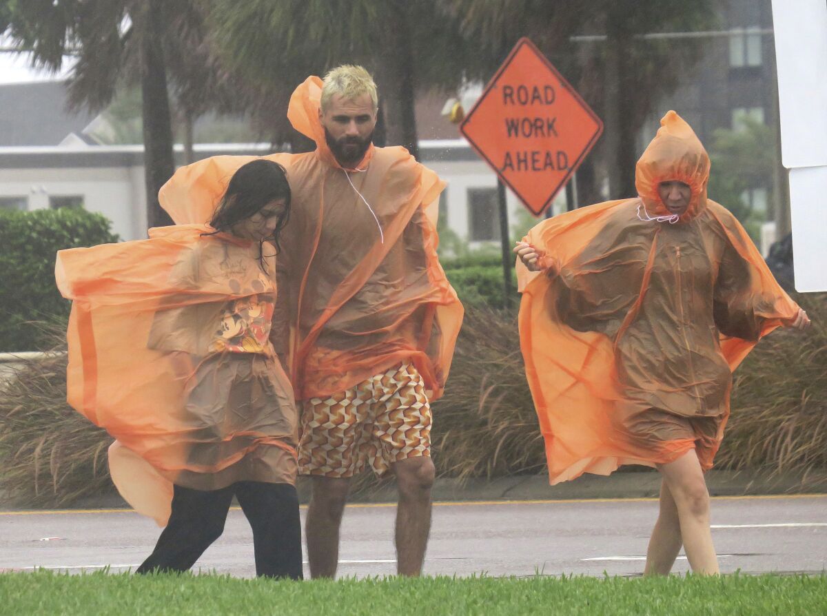 People in raincoats walk along International Drive in Orlando, Fla., Wednesday, Sept. 28, 2022, as the first effects of Hurricane Ian are felt in central Florida. (Joe Burbank/Orlando Sentinel via AP)