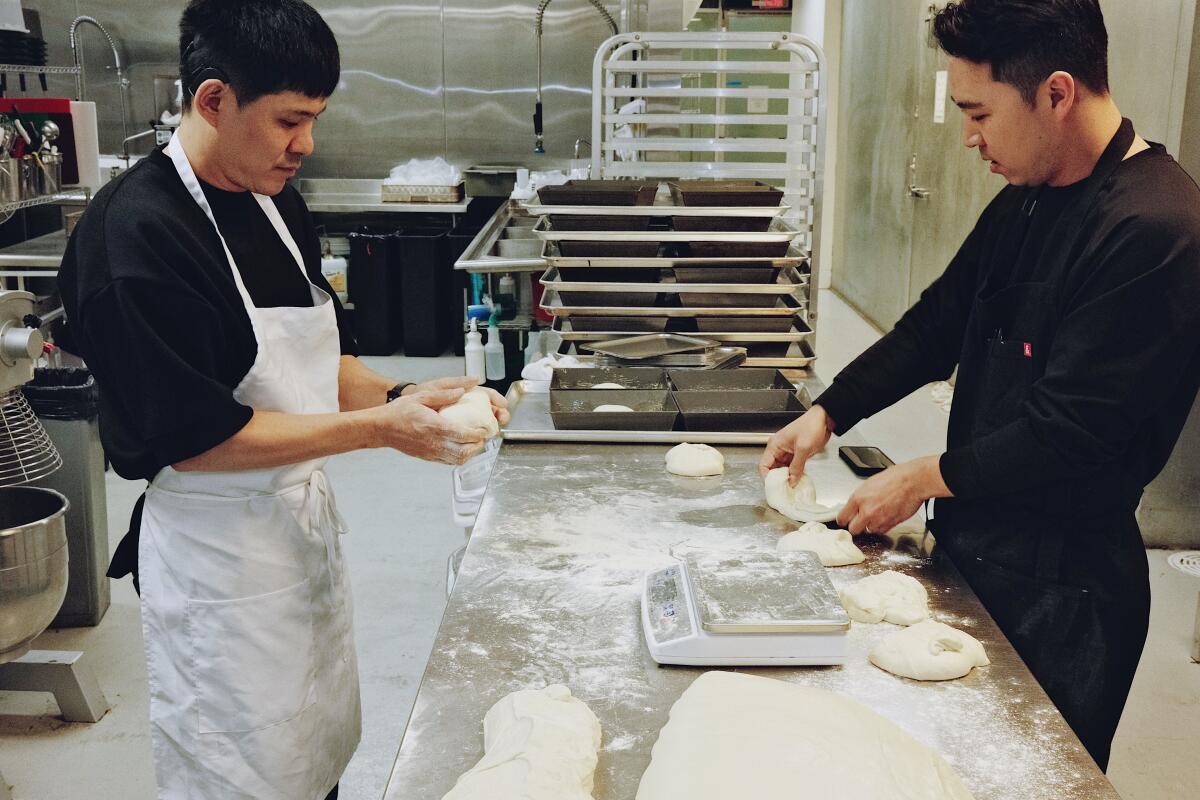 Two men in a restaurant kitchen making pizza dough