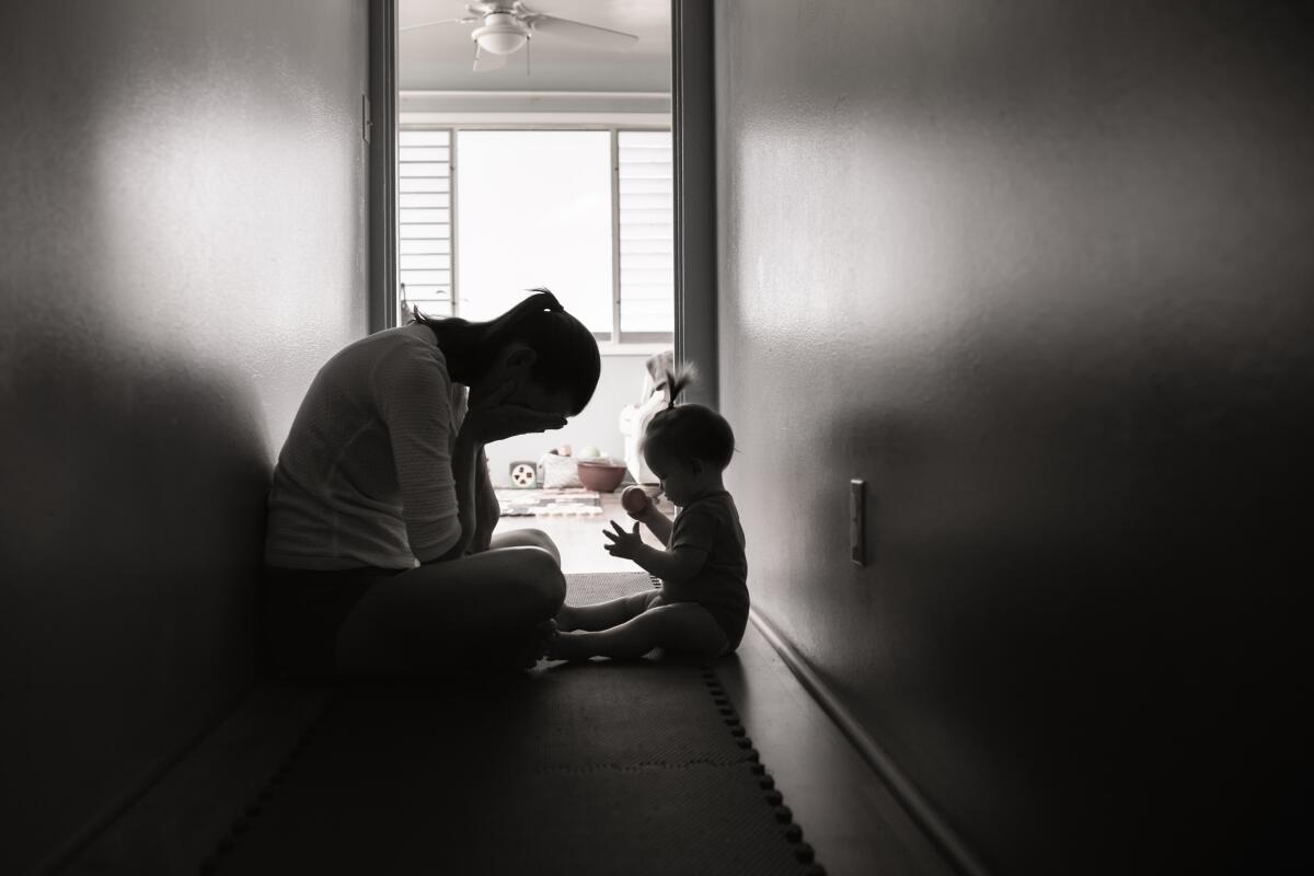 A silhouette of a woman sitting in a hallway with her head in her hands, across from a baby
