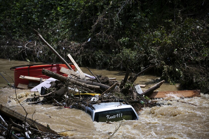 A pile of large debris including a partly submerged truck washed away by muddy, turbulent floodwaters
