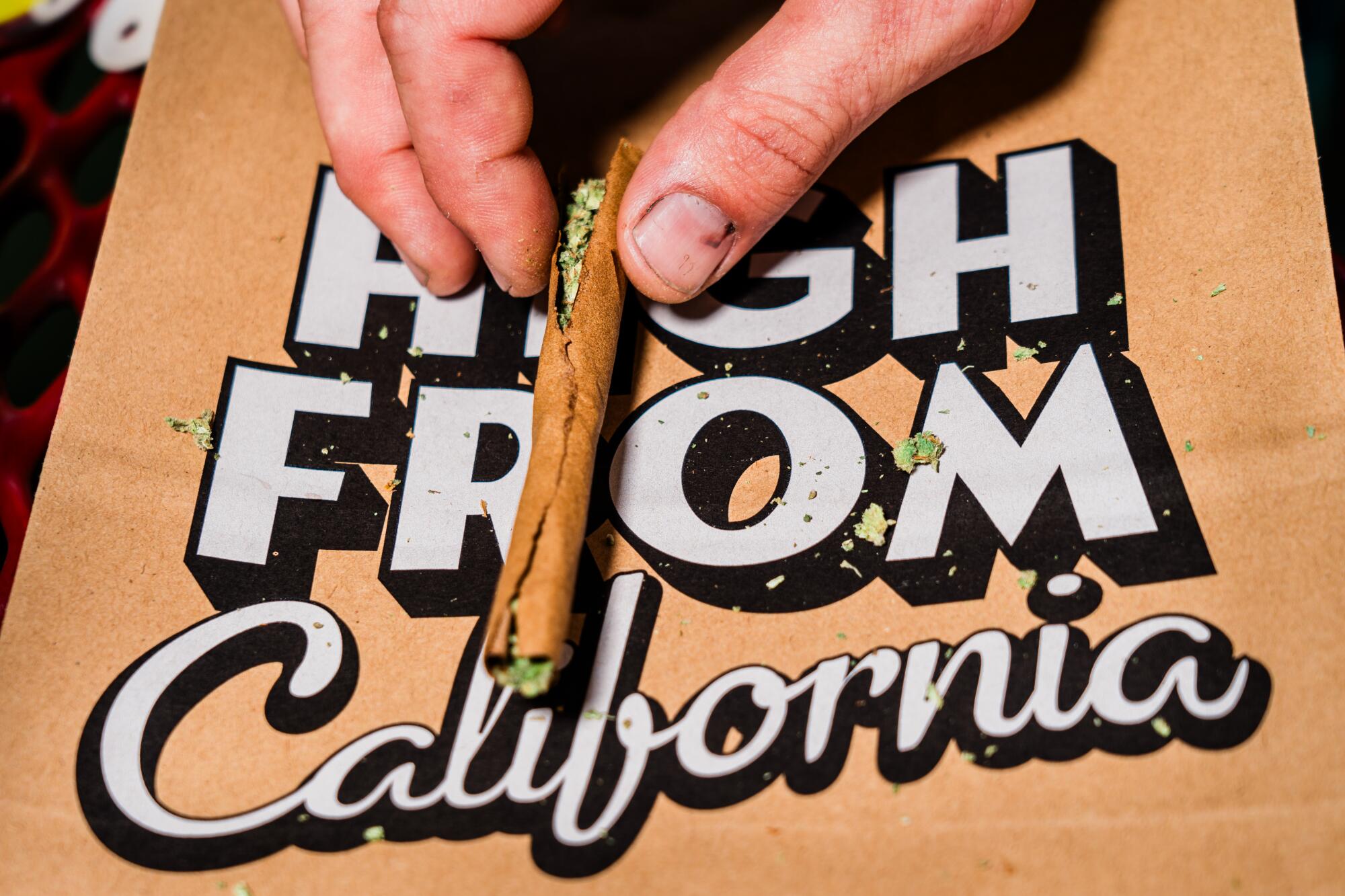 A cannabis joint in front of a bag that reads "High from California"