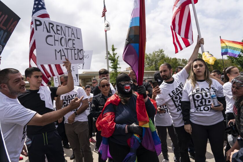 Una mujer envuelta en una bandera del Orgullo LGBT rodeada por personas que protestan contra los eventos por el mes del Orgullo LGBT de la escuela primaria Saticoy, en Los Ángeles, el viernes 2 de junio de 2023. (AP Foto/Jae C. Hong)
