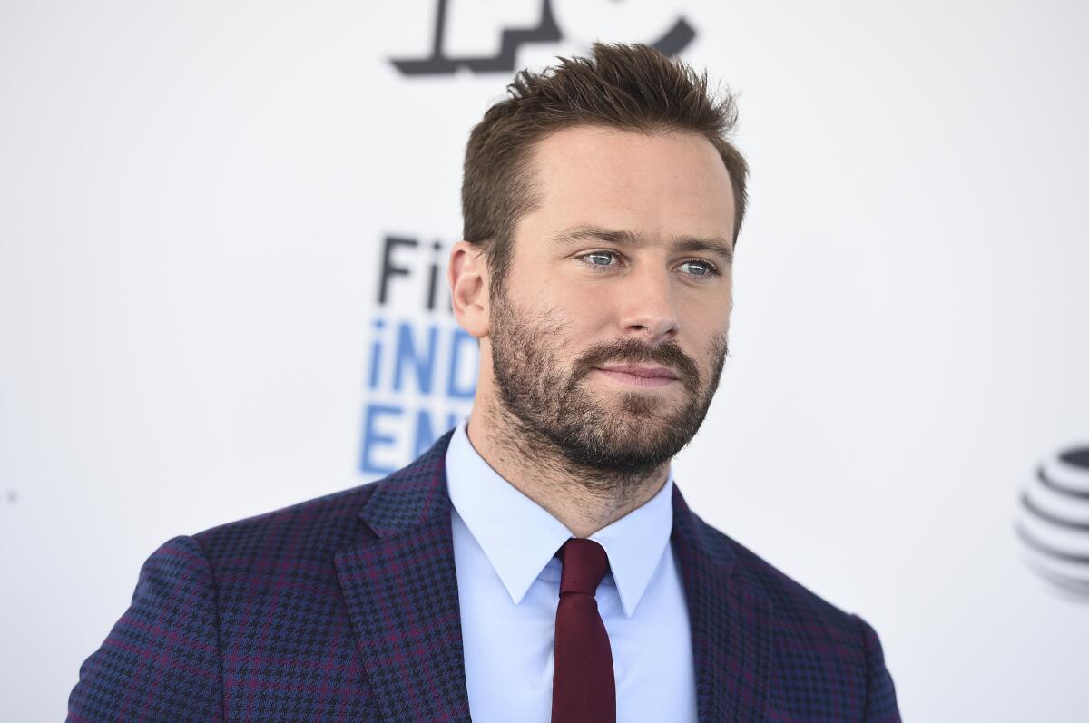 Armie Hammer looking serious in a blue suit, light shirt and maroon tie