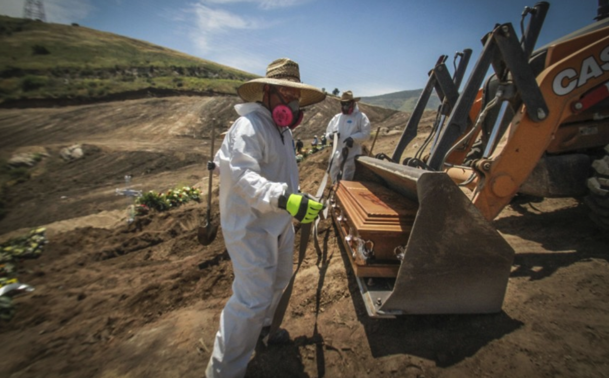 Trabajadores con equipo de protección descargan un ataúd con los restos de una persona que murió por coronavirus.