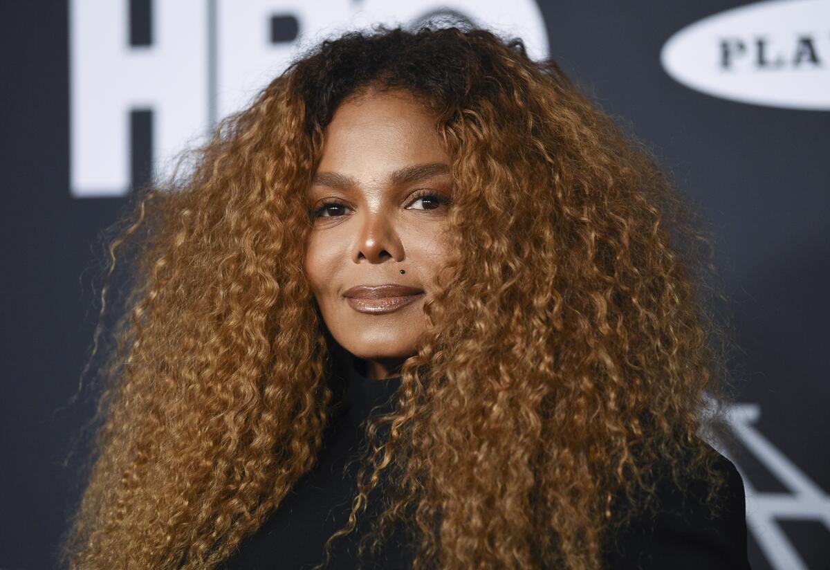 Janet Jackson poses with voluminous ginger-toned hair in front of a dark backdrop