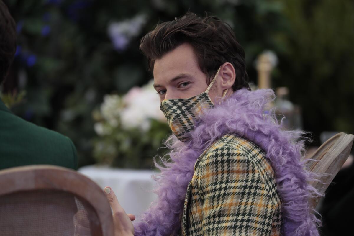 A man with brown hair in a plaid mask, matching blazer and purple boa