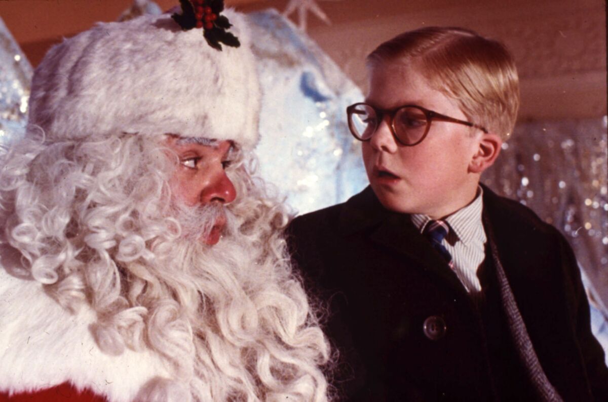 A boy wearing glasses and a suit talks to Santa Claus.