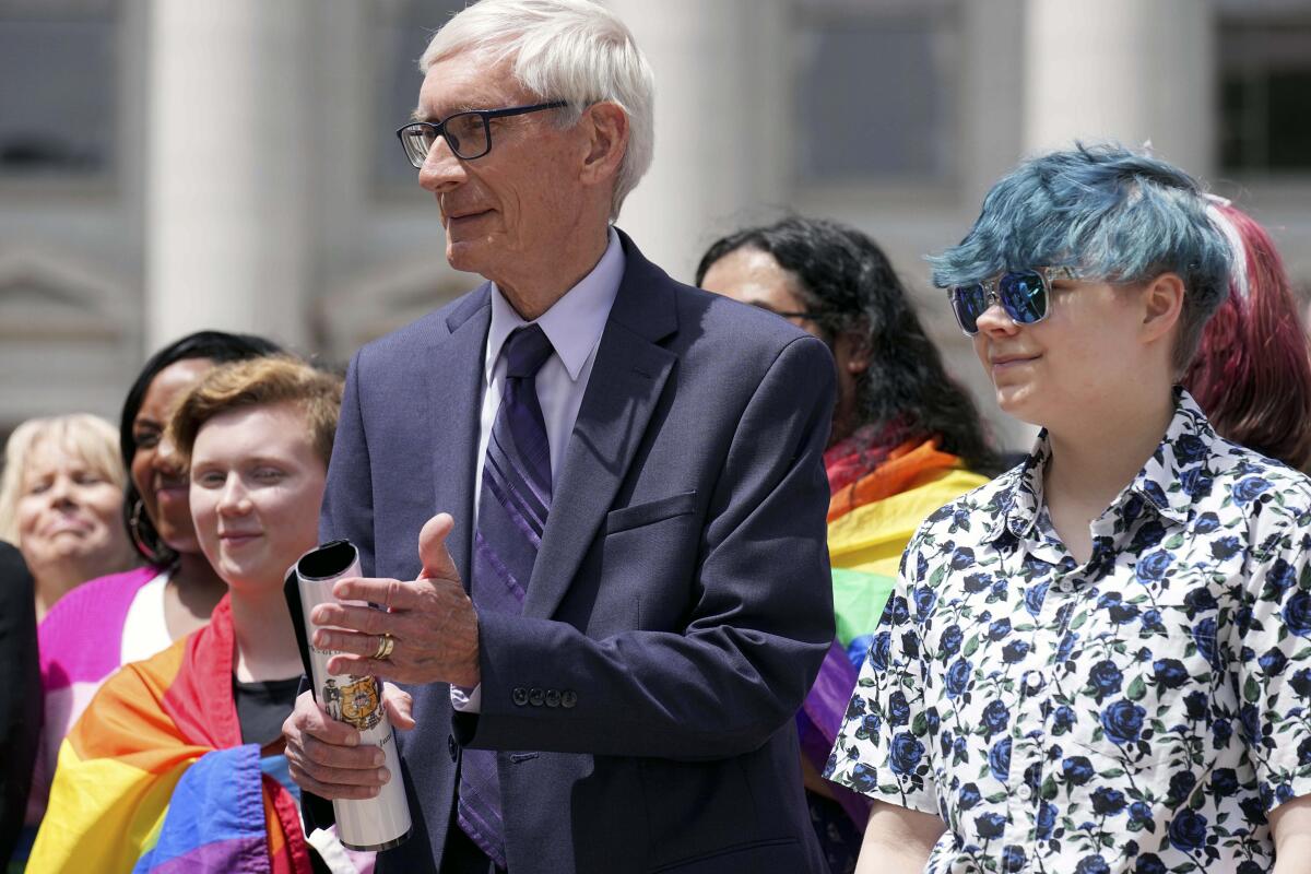 Wisconsin Gov. Tony Evers, left, stands next to 16-year-old Aspen Morris at the Rainbow Pride flag raising Wednesday, June 1, 2022 at the Capitol in Madison, Wis. The symbol of lesbian, gay, bisexual and transgender pride will be flown over the Capitol's East Wing in recognition of LGBTQ Pride Month, which runs until the end of June. In June 2019, Evers issued an executive order to raise the pride flag above the state Capitol for the first time in Wisconsin history. This is the fourth year the flag has flown below the U.S. and state flags on the east-wing flagpole. (Mark Hoffman/Milwaukee Journal-Sentinel via AP)