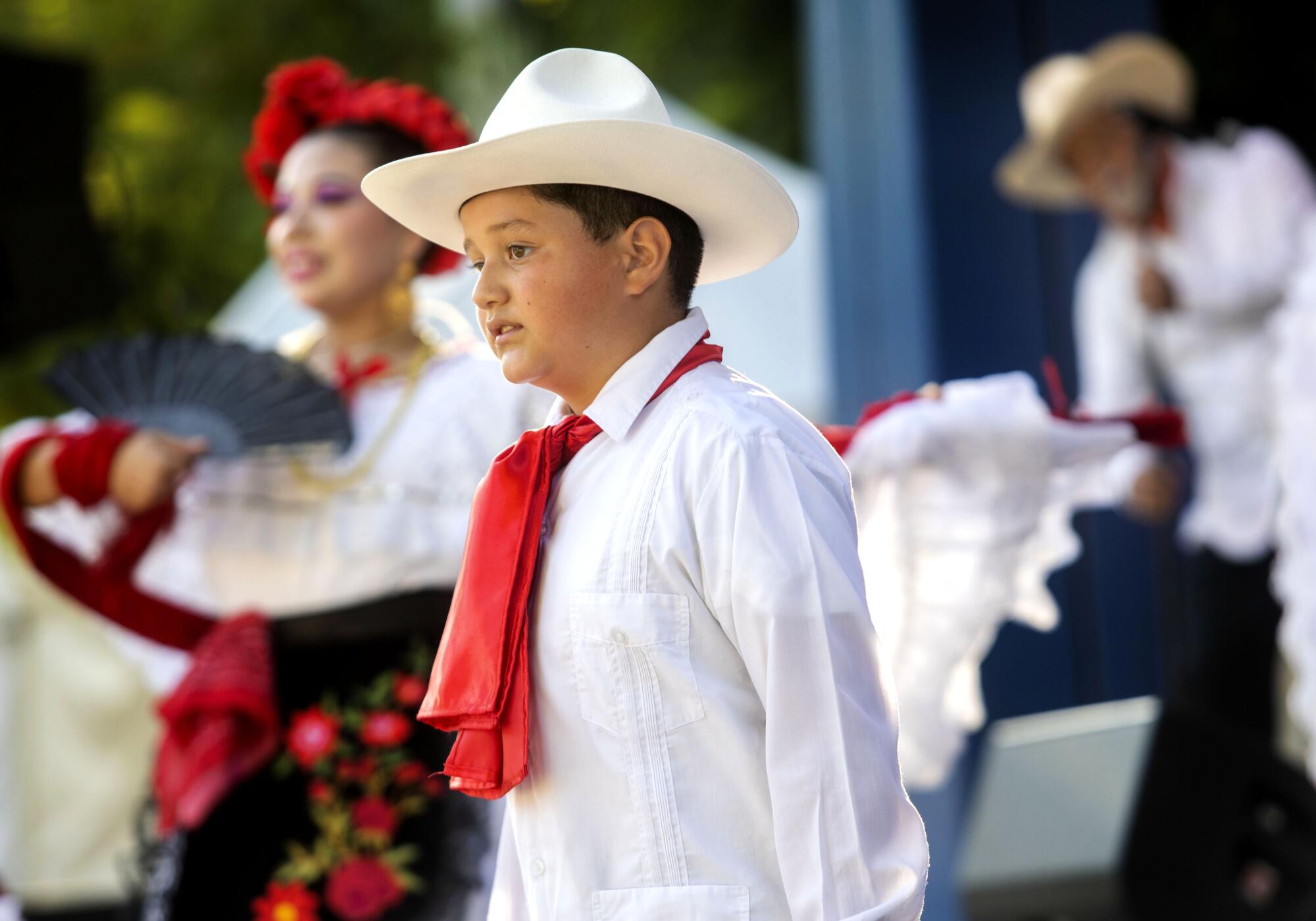 Vincent Mendoza, 10, dances with other dancers. He's wearing a white outfit and a red traditional tie.