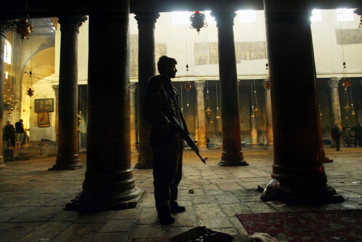 ON GUARD: A Palestinian passes through the sanctuary of Bethlehem's Church of the Nativity during the last week of the siege. The men inside prayed twice a day, facing the right wall of the church, toward Mecca. Many slept in the sanctuary under blankets with their assault rifles near their heads. They cooked meals of weed soup and fried leaves.