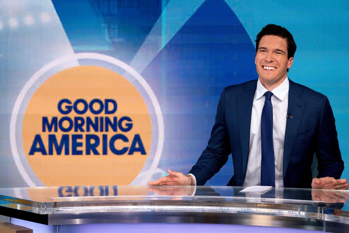 A smiling Will Reeve in a dark blue suit and tie, behind a desk with a "Good Morning America" logo to his right
