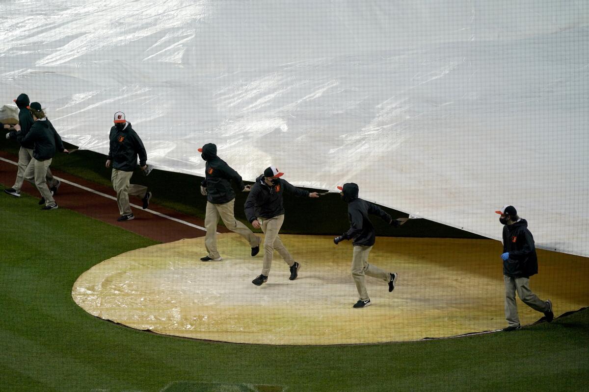 Grounds crew members place a tarp over the infield at Oriole Park at Camden Yards prior to a baseball game between the Baltimore Orioles and the Seattle Mariners, Monday, April 12, 2021, in Baltimore. (AP Photo/Julio Cortez)